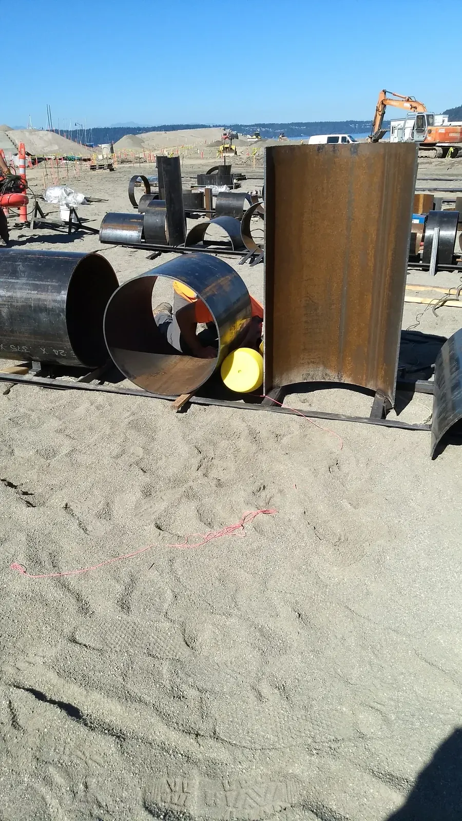 A worker beside a large circular pipe section and a tall curved segment set on steel supports.