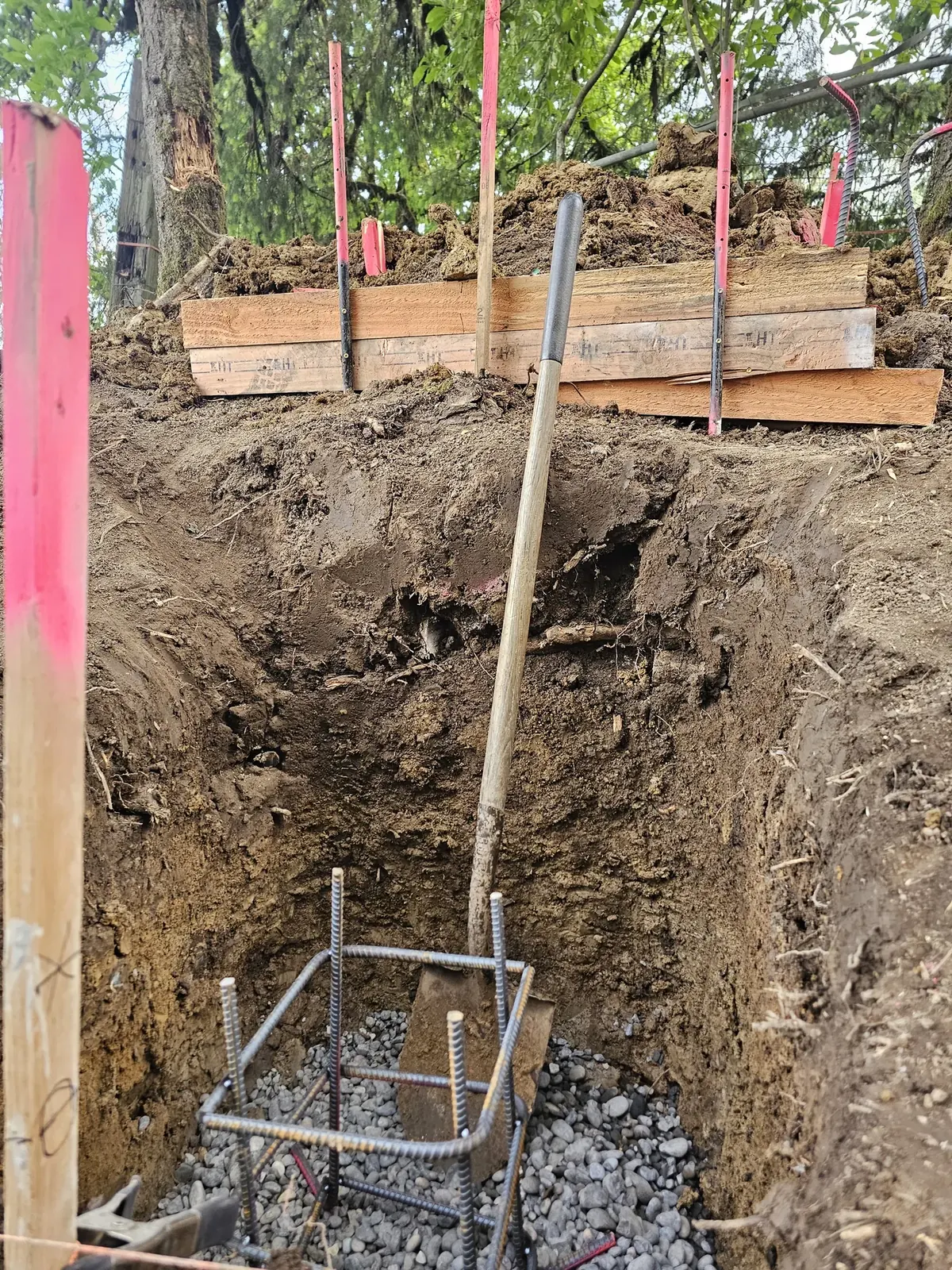 A reinforcing steel cage extends into a post excavation with gravel at its base.