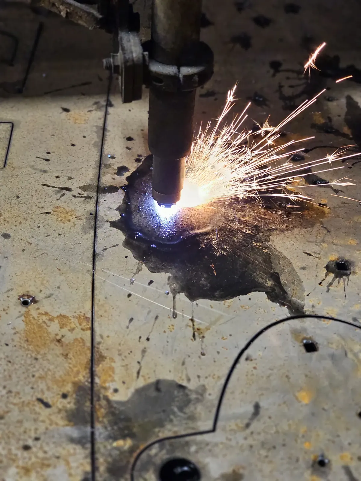 Sparks fly from the plasma torch as it cuts the steel sign panel on the cutting table.