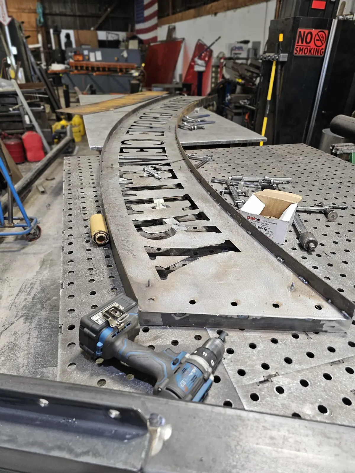 The curved Cherry Grove Cemetery lettering panel, frame and mounting studs on a fabrication table.