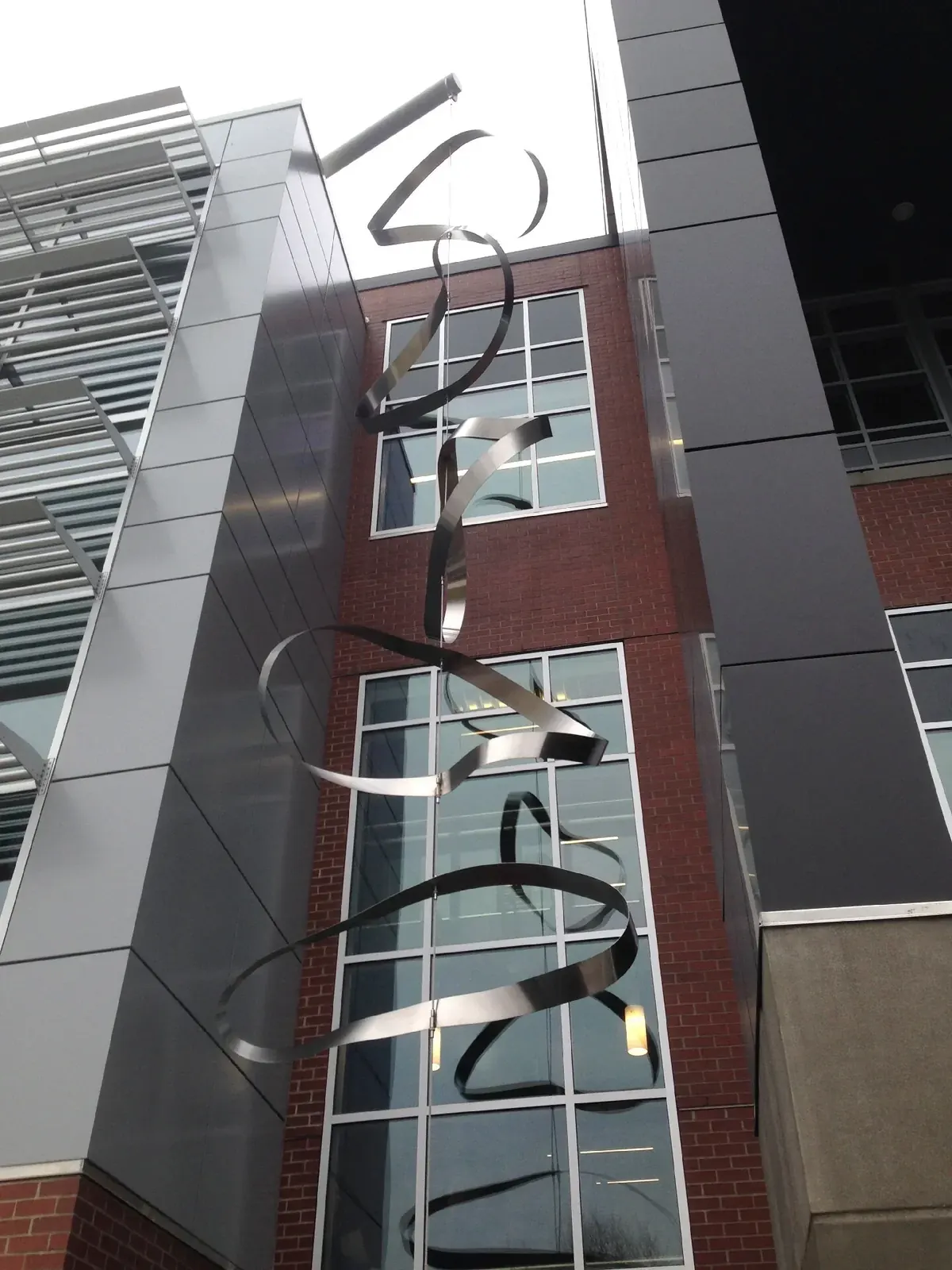 Upward view of the hanging steel rings, central suspension cable, and reflections in the STEM Building windows.