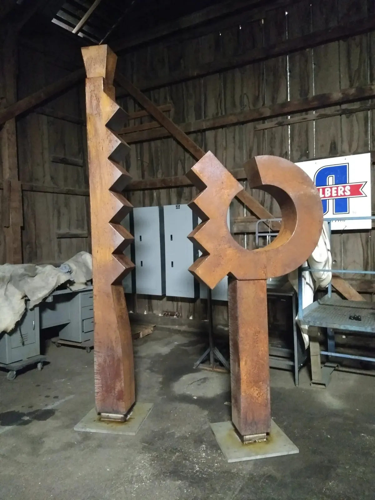 Two completed steel sculptural forms in the WIW shop: a tall stepped column and a shorter circular form.
