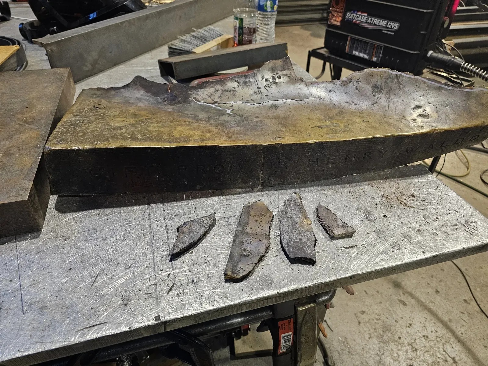 A fractured section of the original base on a workbench, with several loose metal fragments in front.