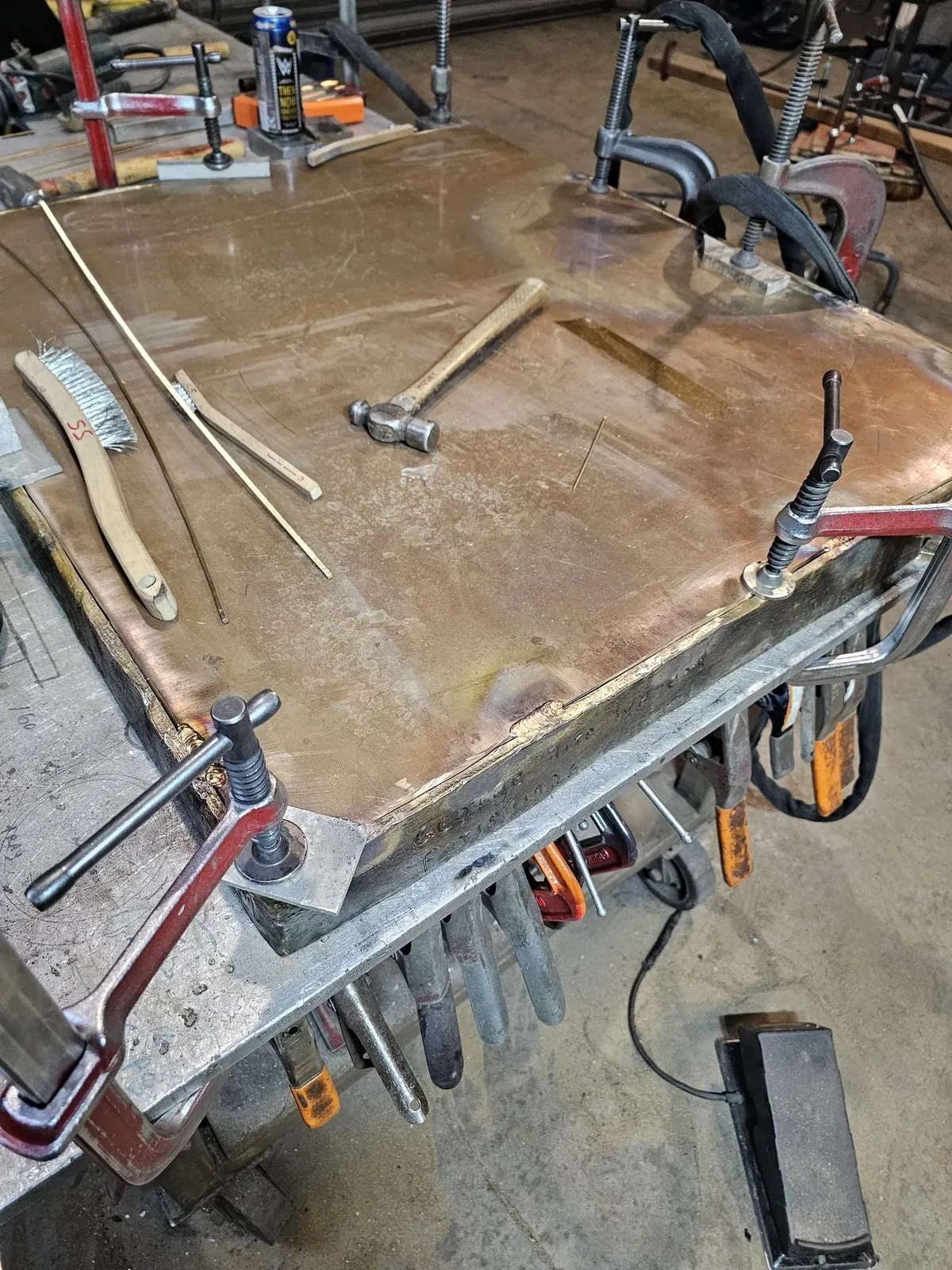 A new rectangular metal plate held with clamps inside the original inscribed sidewalls on a workbench.