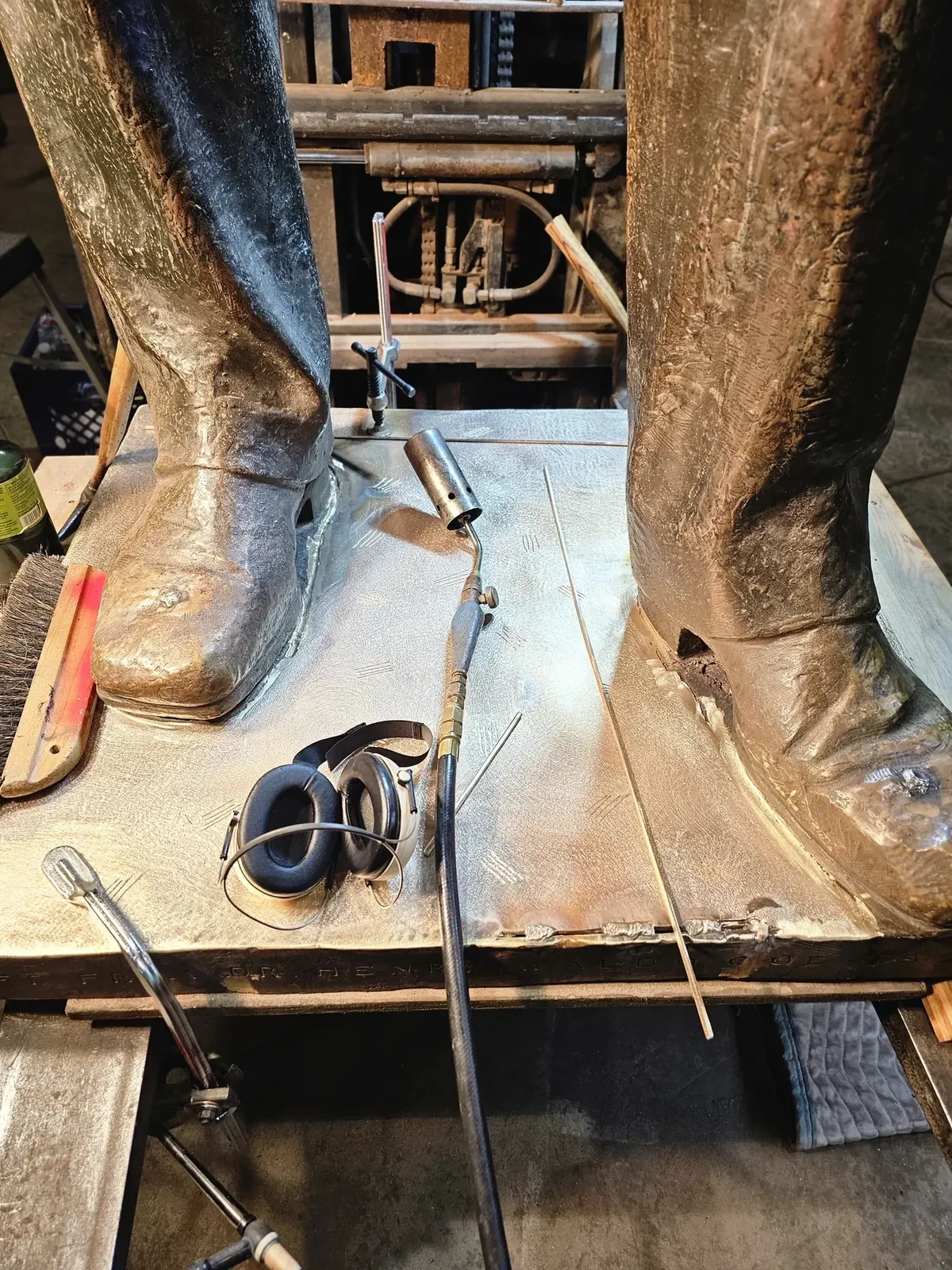 Both original bronze feet on the new base, with welding and finishing tools resting on the plate.