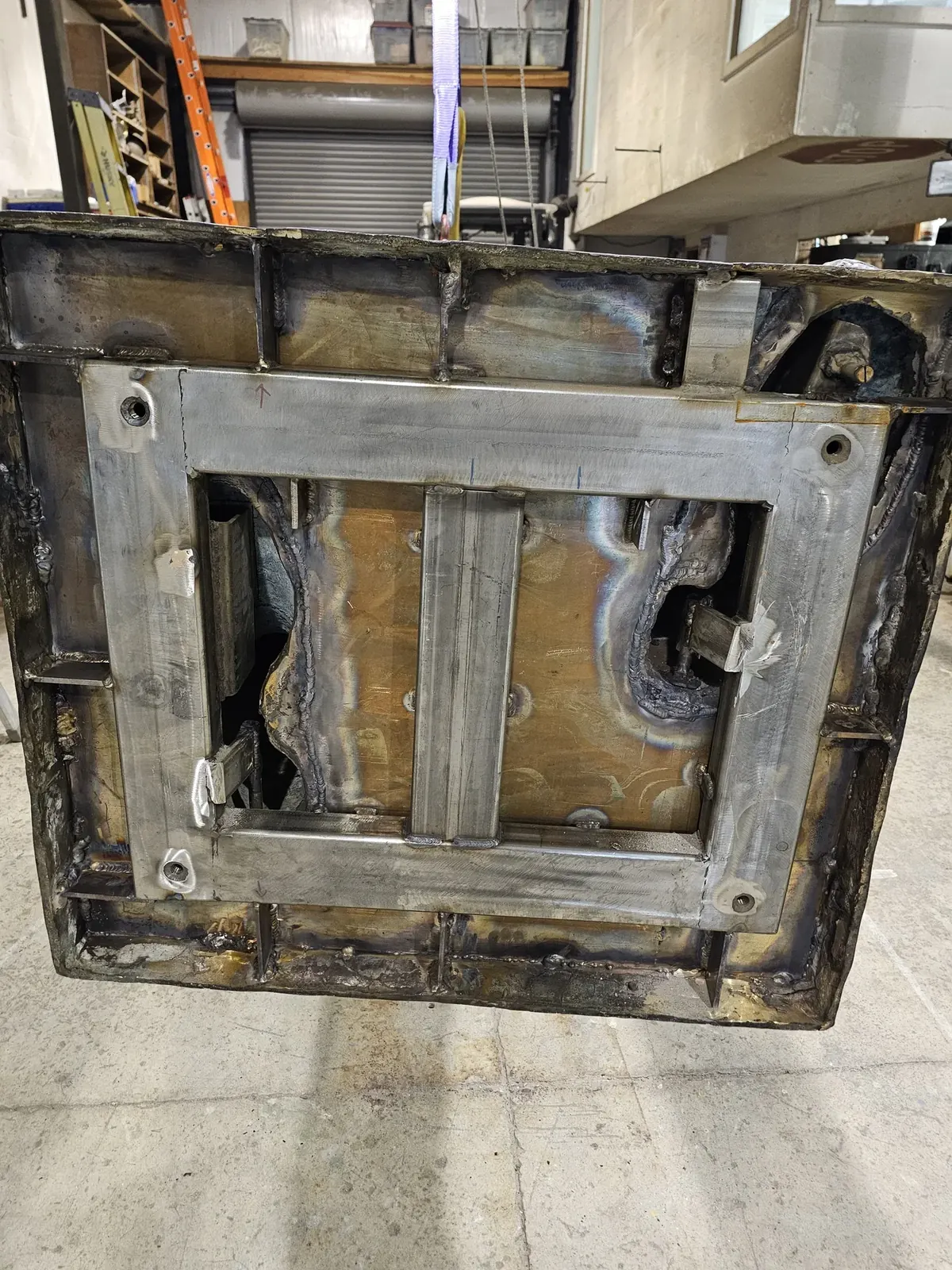 Underside of the rebuilt base, showing the stainless steel frame, central member, connections, and retained original outer sides.