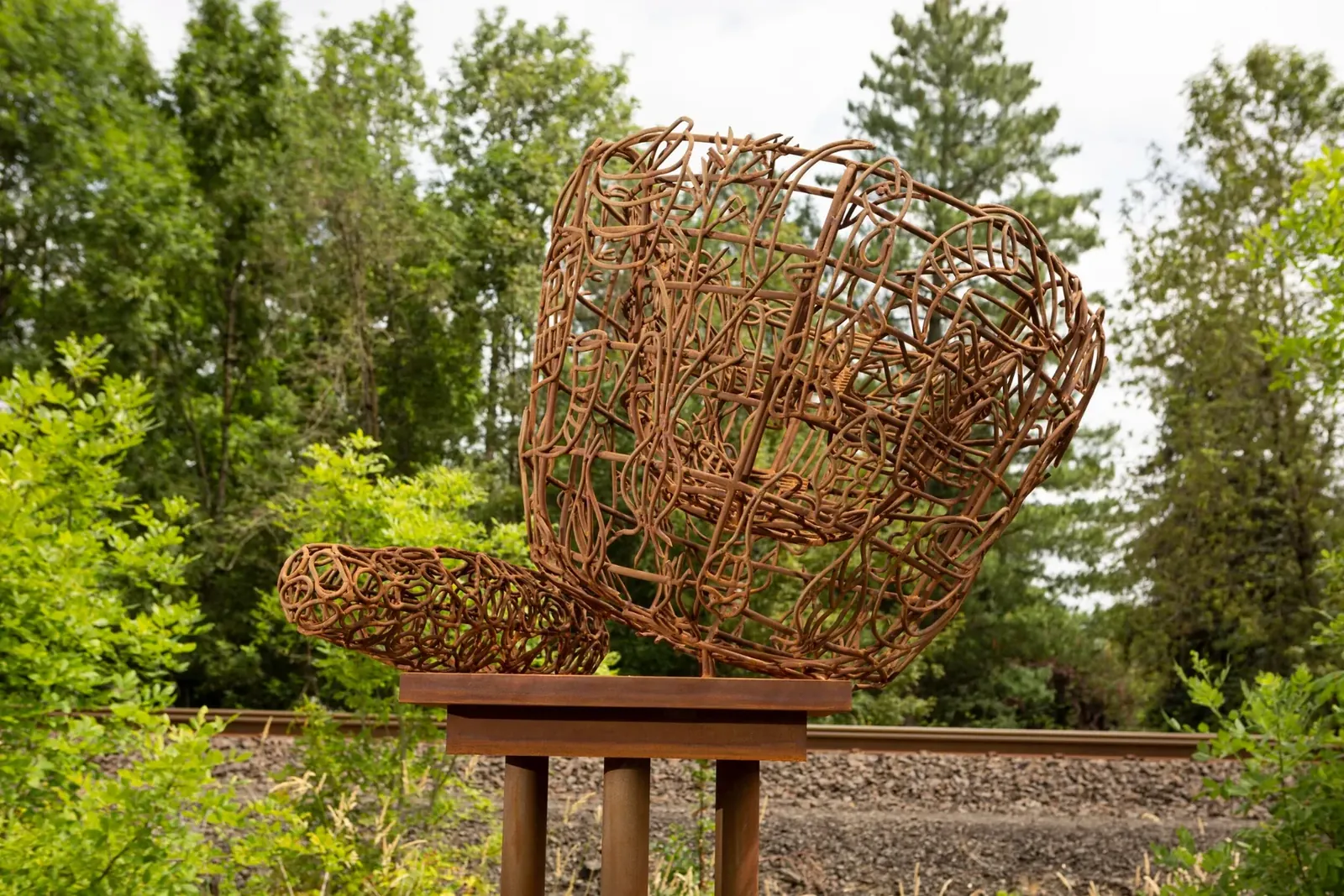 Detail of Live, showing the mortar and pestle shape and plant and tool motifs within its rust-colored steel framework.