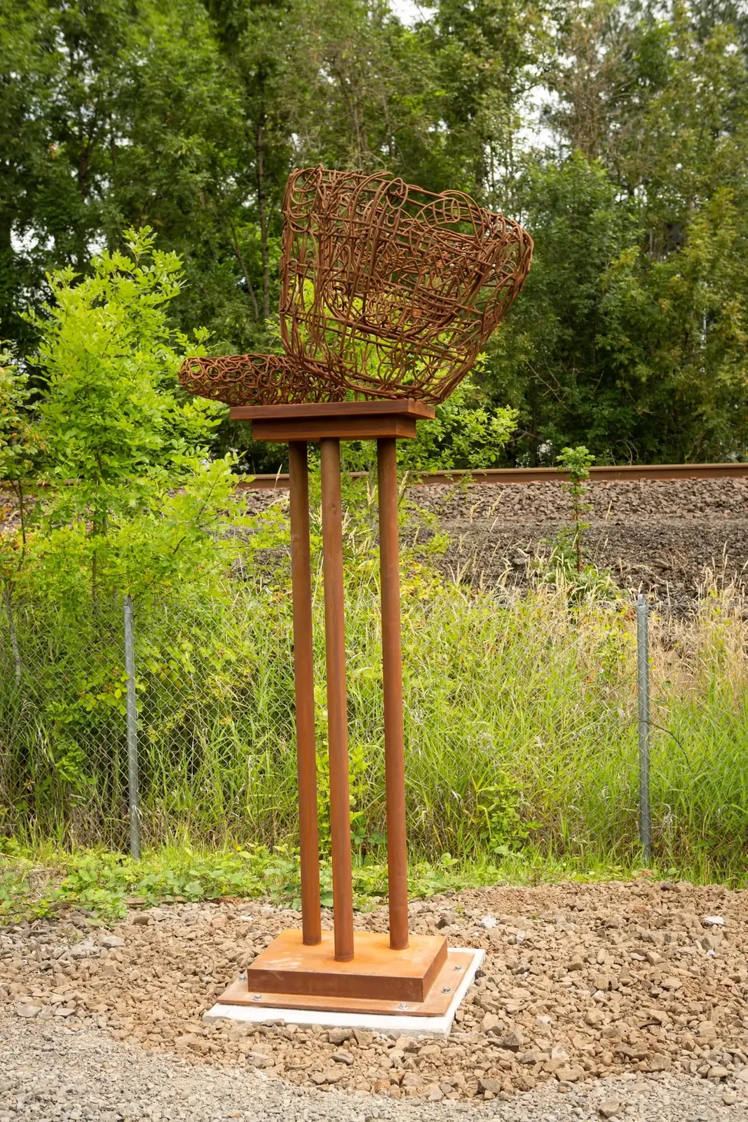 Live, an open steel mortar and pestle on a tall three-column pedestal beside the Tigard Outdoor Museum trail.