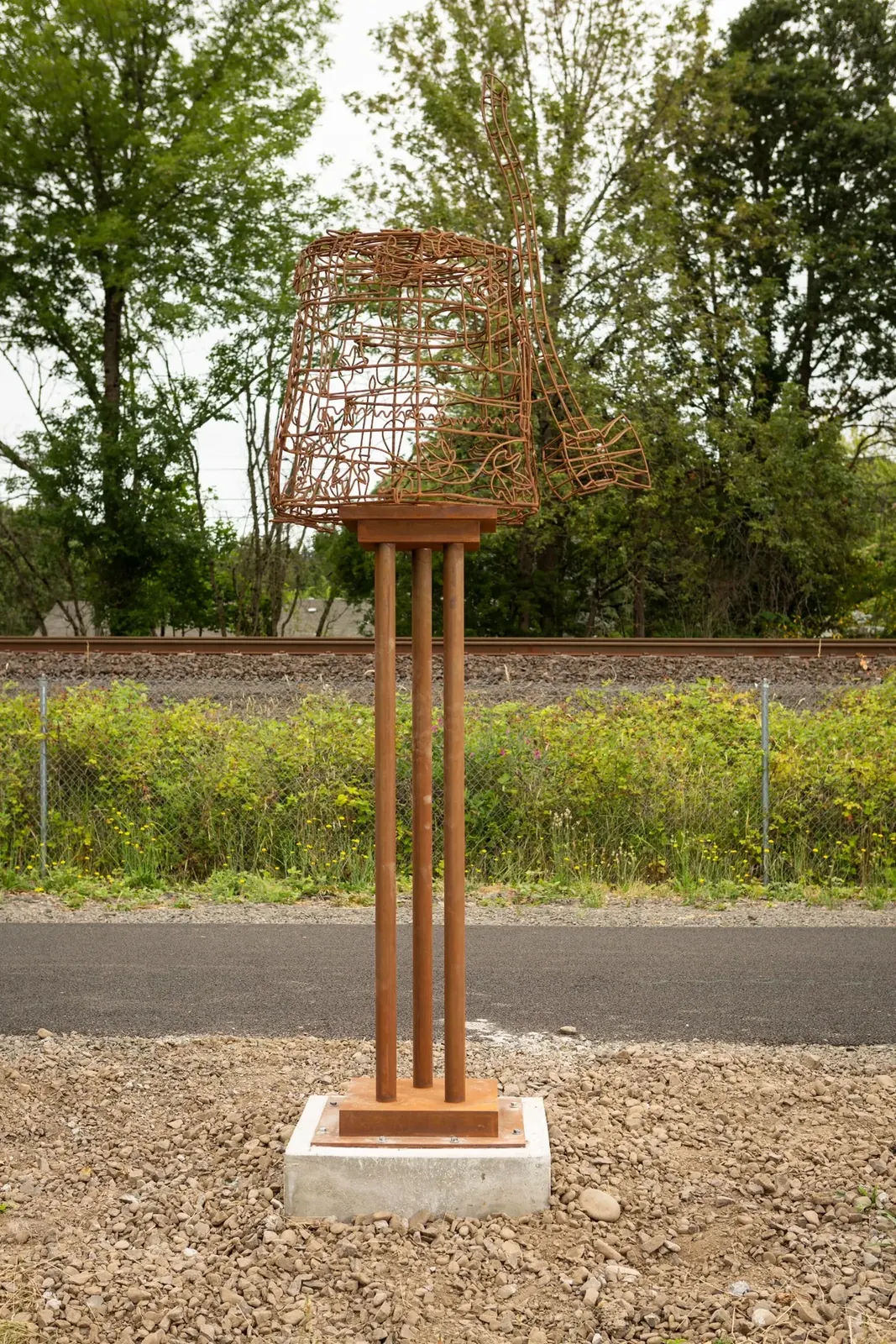 Settle, a steel stump and axe sculpture on a tall pedestal beside the paved trail and railroad.