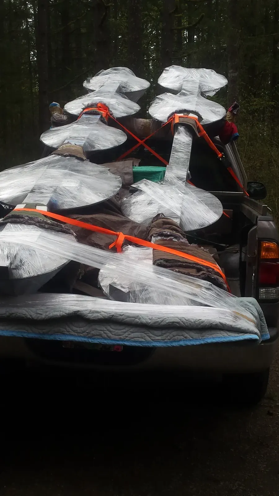 Circular metal housings wrapped in protective material and secured with orange straps in the back of a pickup.
