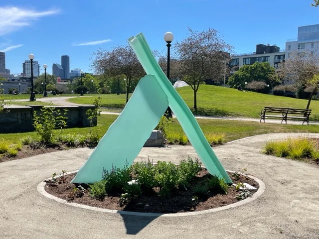 Two angled glass forms meet above a planted bed, forming Lambda in Cal Anderson Park.