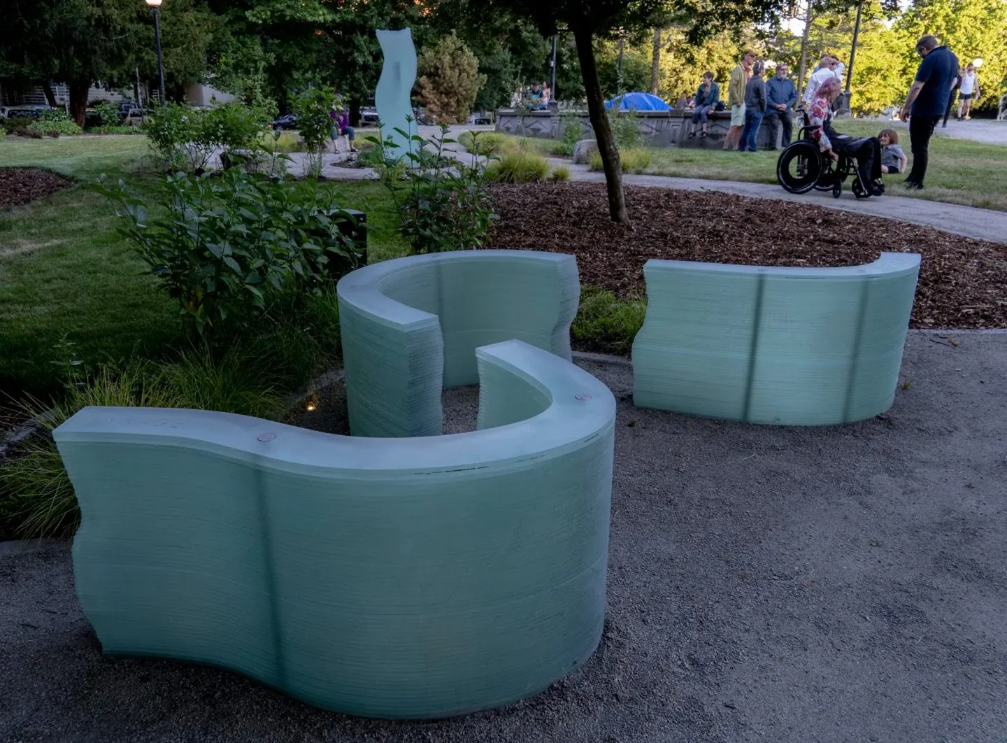 Reverie, the curved stacked glass sculpture, with visible stainless hardware and caps; visitors and Monolith are in the background.