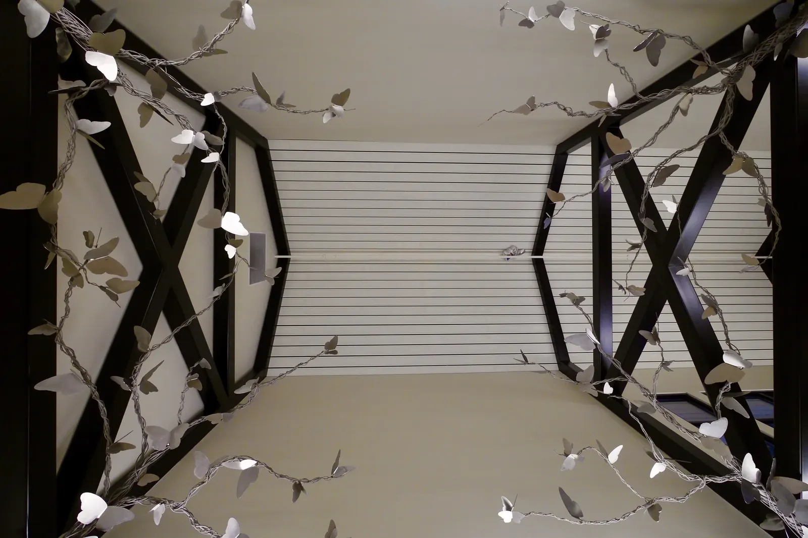View straight up between the ceiling beams, with branching stainless steel butterfly forms extending into the space from both sides.