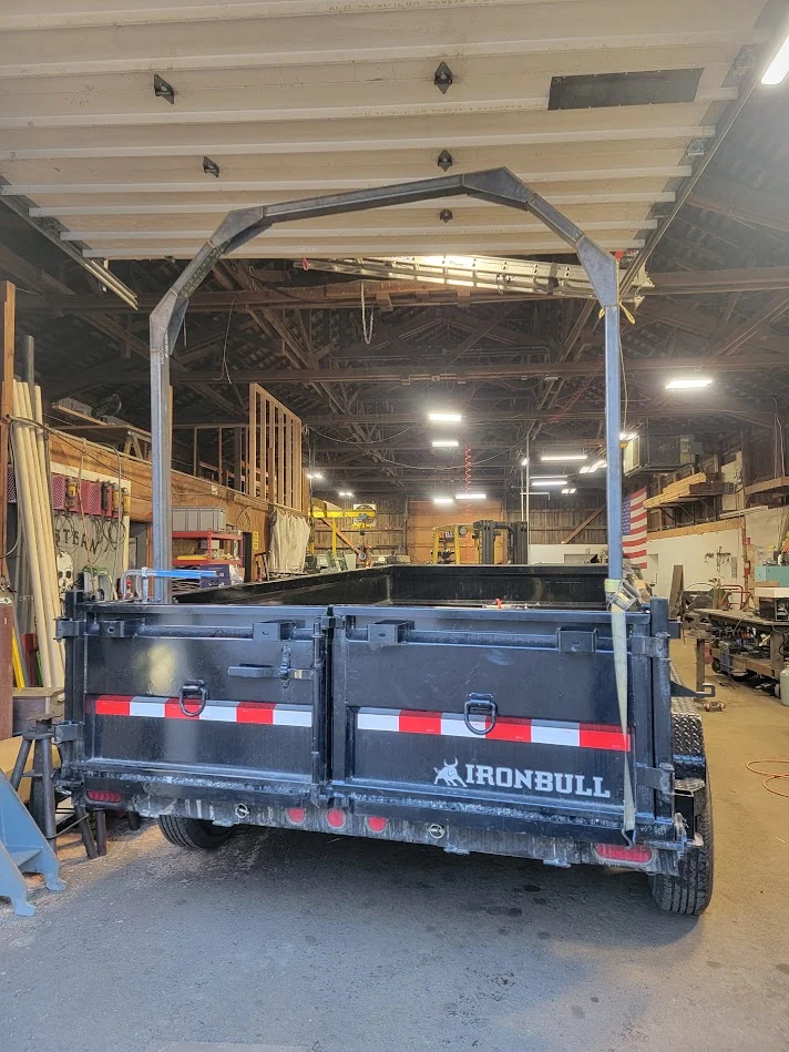 Unpainted log-loader frame rising above the back of a dump trailer
