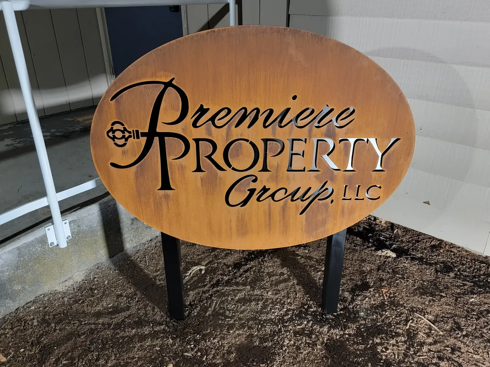 Oval Premiere Property Group metal sign with cut-out script lettering and a key graphic