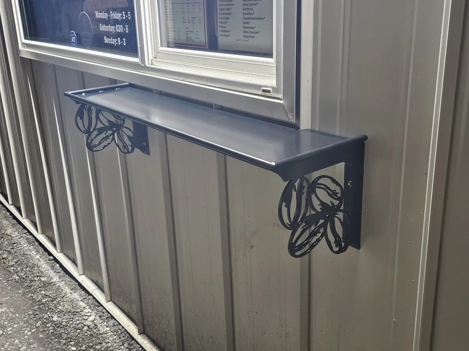 Dark metal service shelf mounted beneath a coffee stand window
