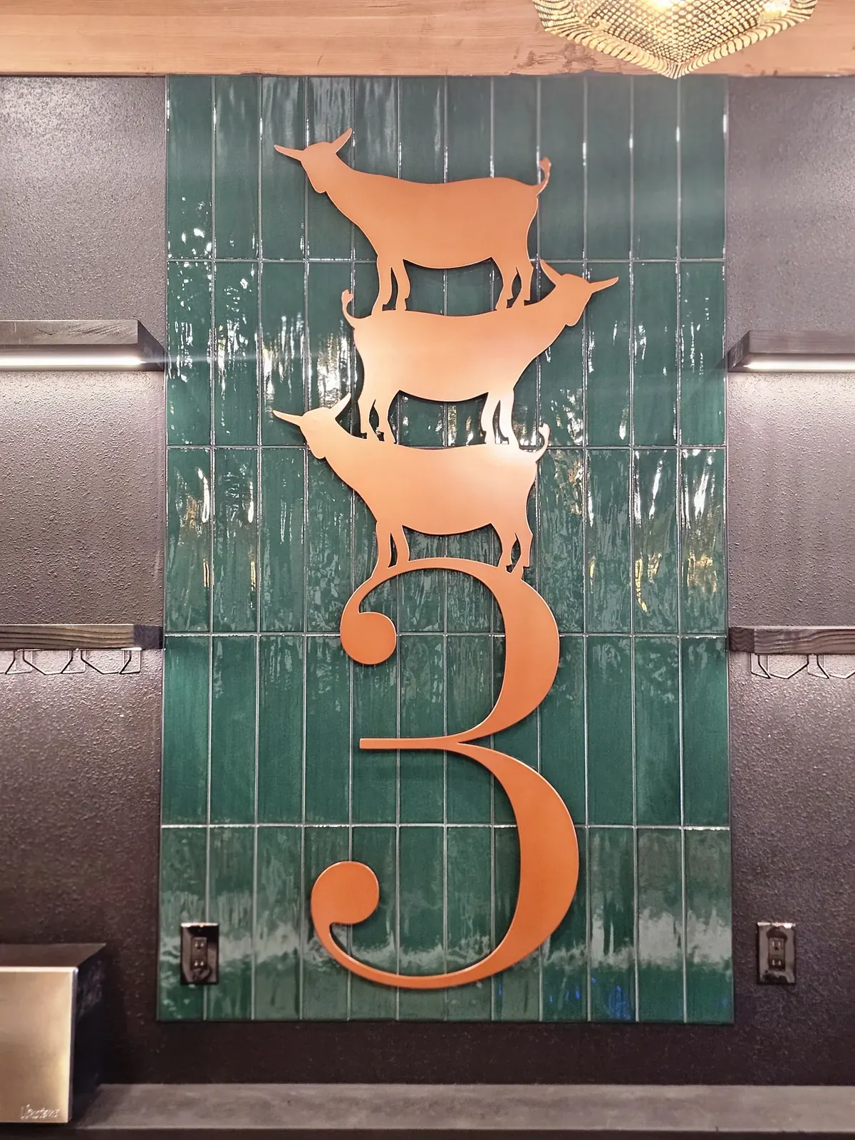 Metal wall sign with three stacked goat silhouettes above a large numeral 3