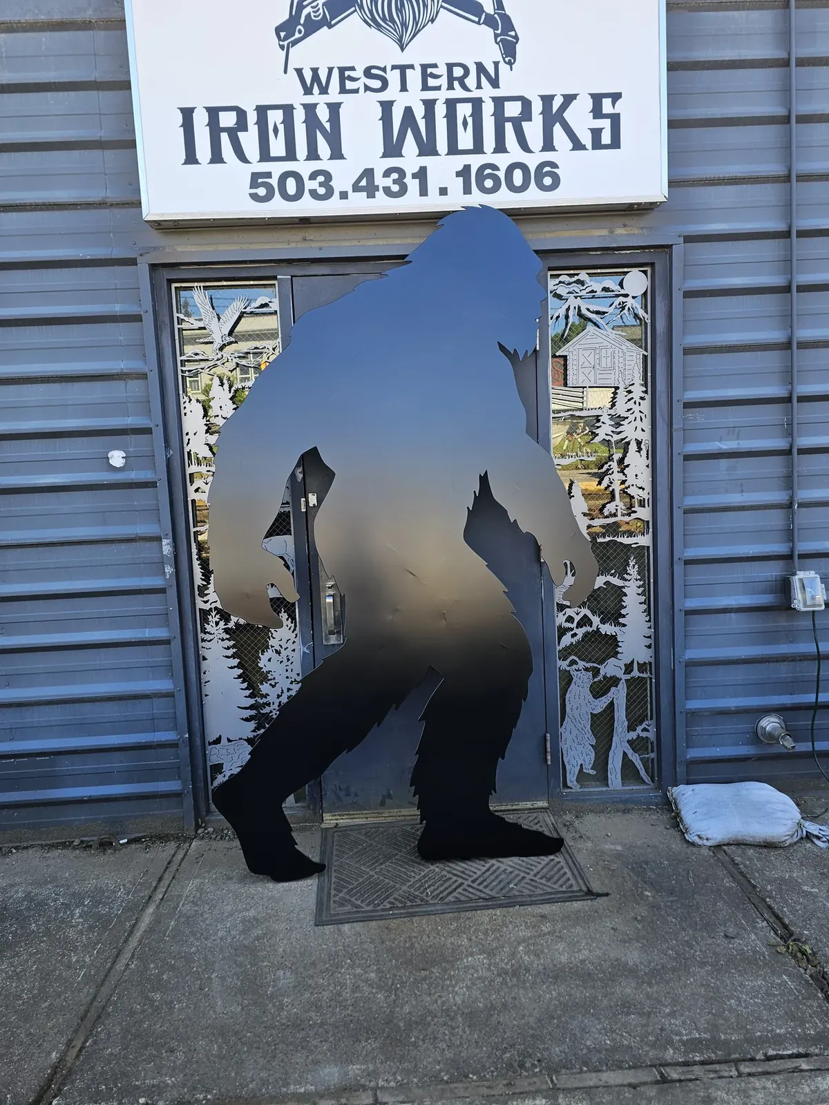 Dark metal Bigfoot silhouette standing outside the Western Iron Works shop