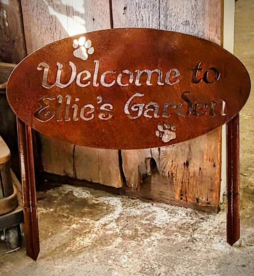 Oval metal sign reading Welcome to Ellie’s Garden with paw-print cutouts and two stakes
