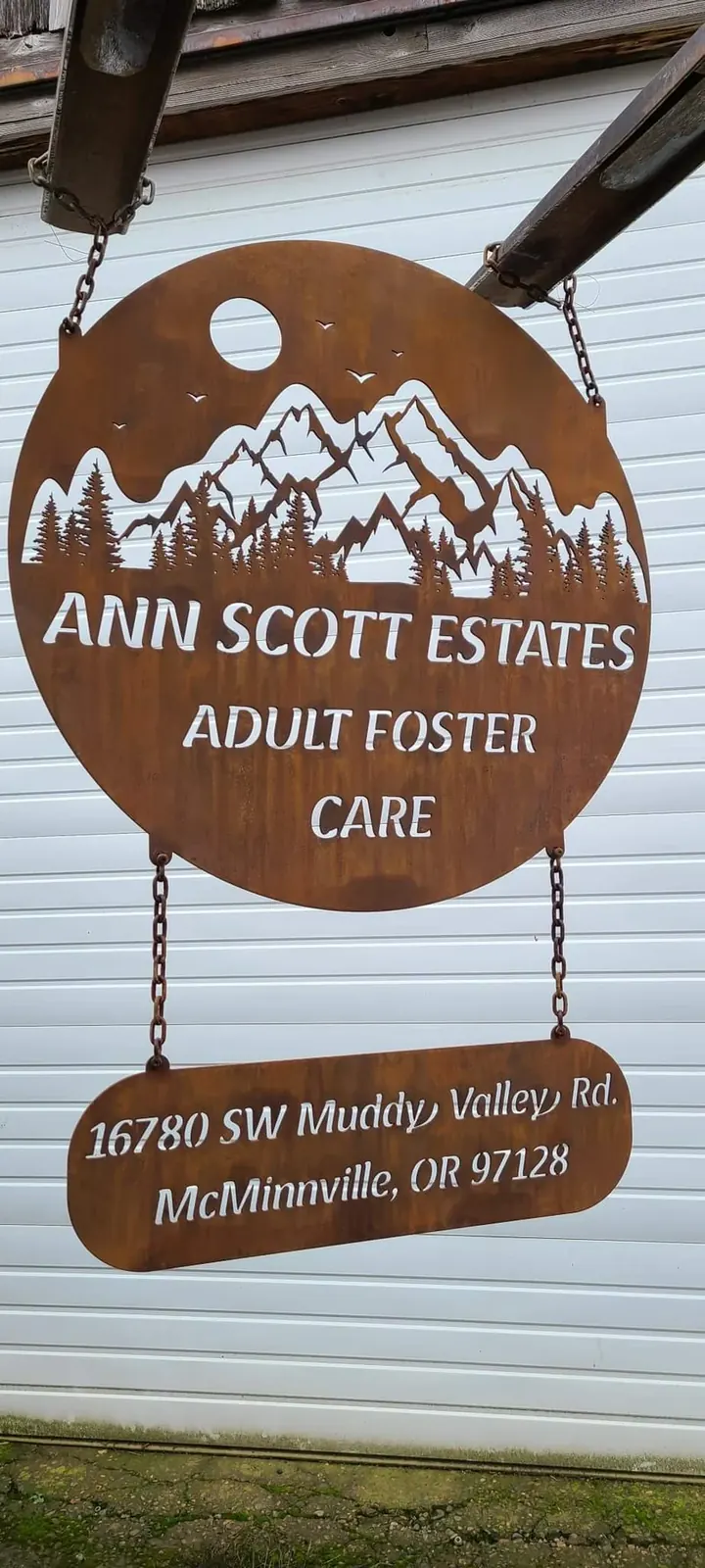 Round Ann Scott Estates Adult Foster Care sign with a mountain graphic and a smaller address panel hanging below