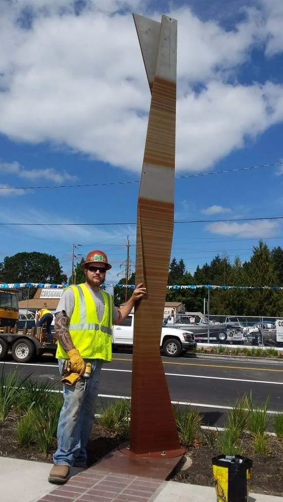 A person stands beside an installed Stratum tower, showing the scale of the sculpture.