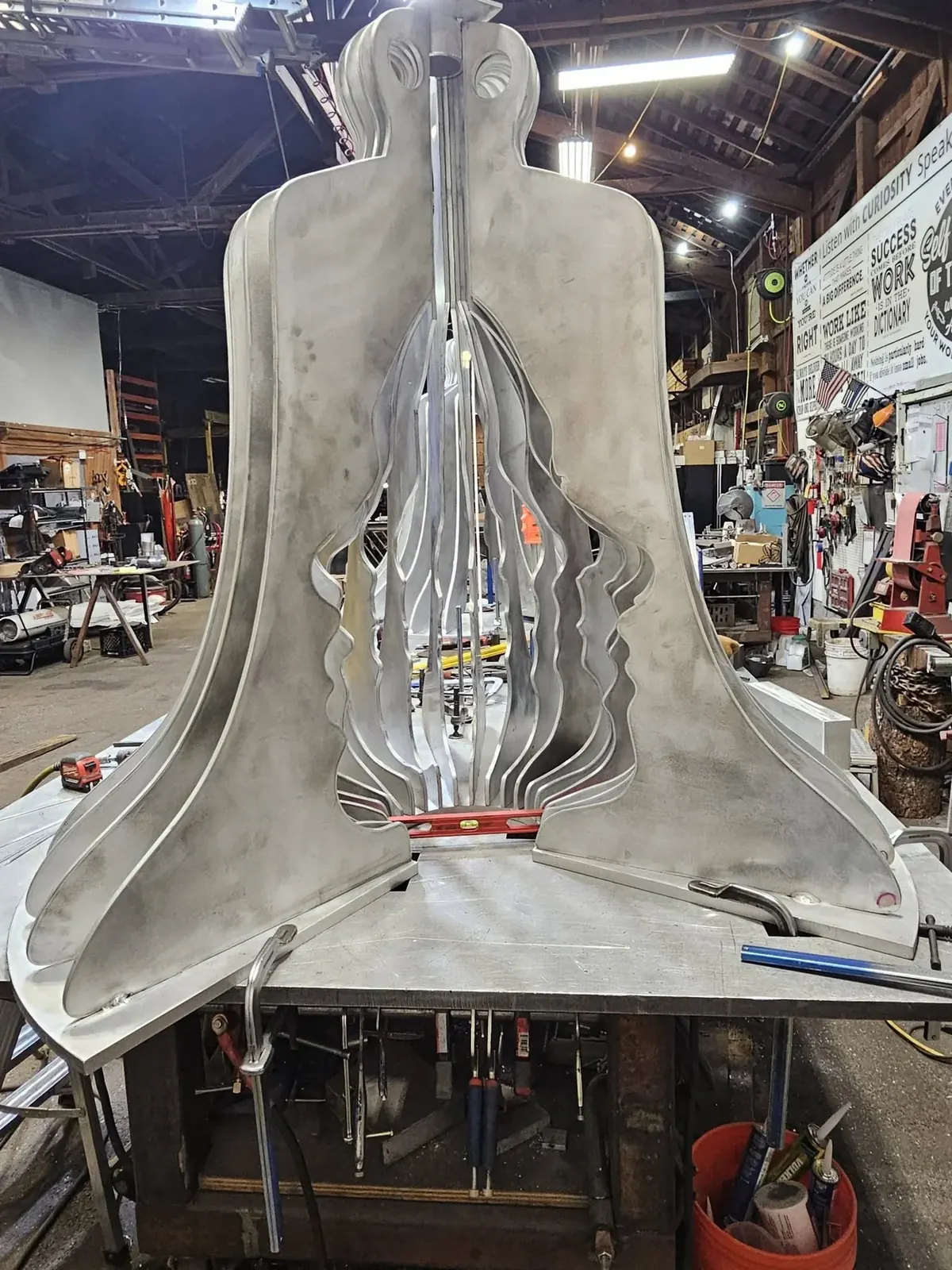A partially assembled aluminum bell with face-shaped profiles visible along the inner edges of its fins.