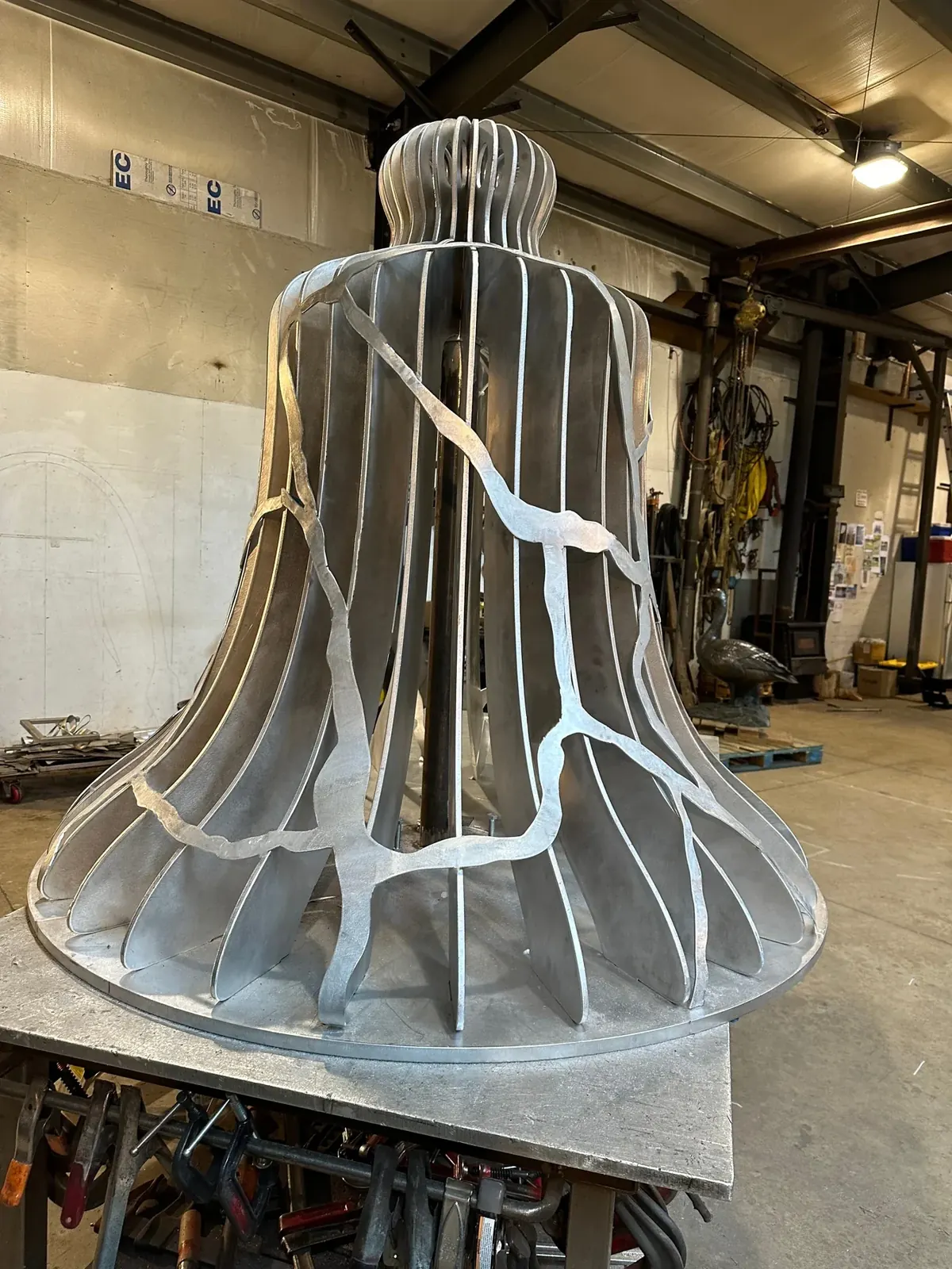 Unpainted aluminum bell on a shop table with branching pieces fitted around its outside.