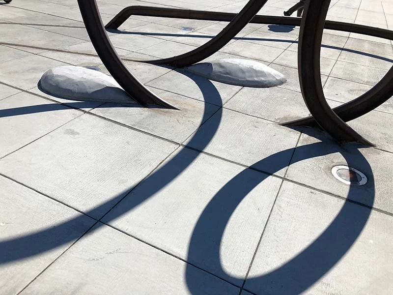 Close view of the steel rail and curved shadows crossing the paving.