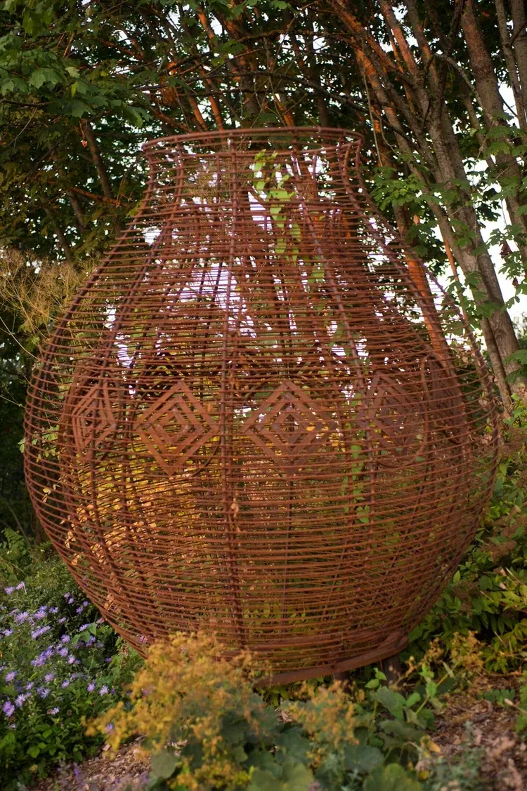Rounded steel basket sculpture with a narrow neck and diamond-shaped motifs visible through its outer steel lines.
