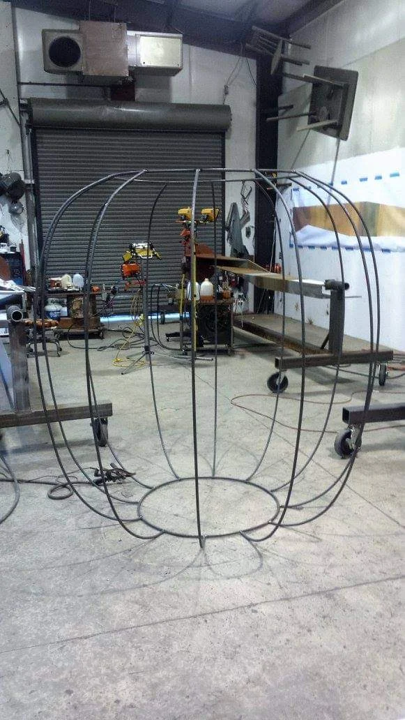 An open basket frame in the fabrication shop, showing widely spaced curved ribs and a circular base.